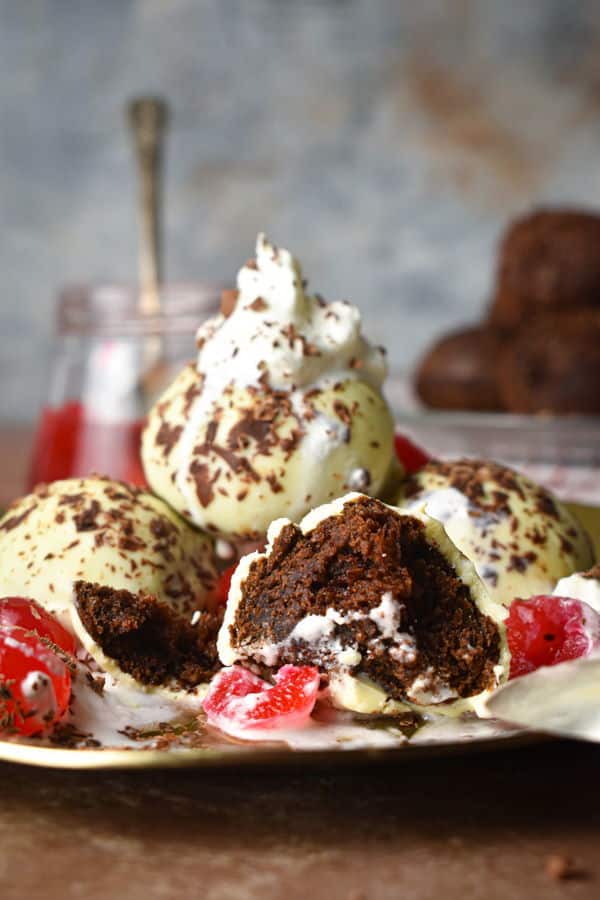 Black forest cake balls on a plate with whipped topping, cherries and chocolate shavings.