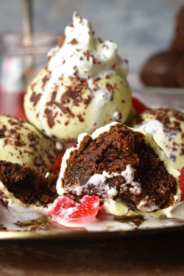 Black forest cake balls on a plate with whipped topping, cherries and chocolate shavings.