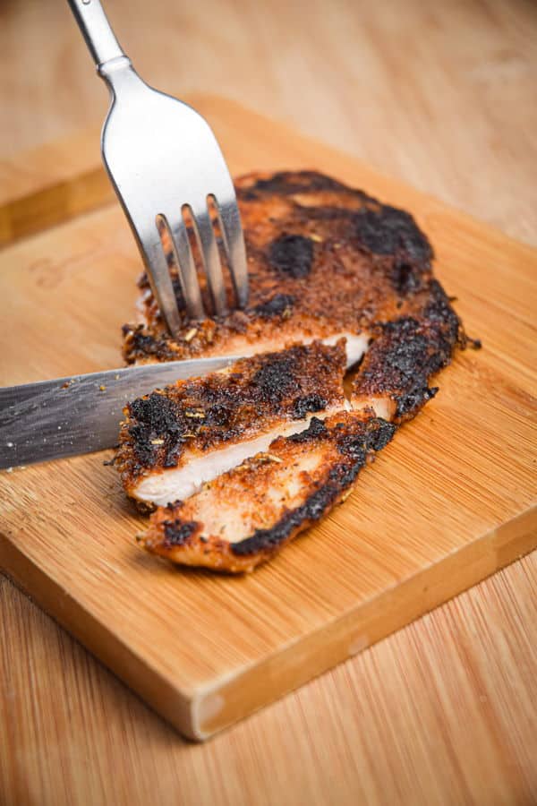 Blackened chicken breast on a cutting board with a fork and knife.