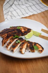 Sliced blackened chicken on a plate with lime wedges.