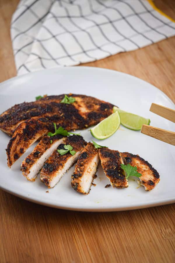 Sliced blackened chicken on a plate with lime wedges.