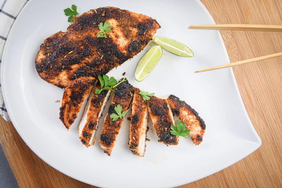 Sliced blackened chicken on a plate with lime wedges.