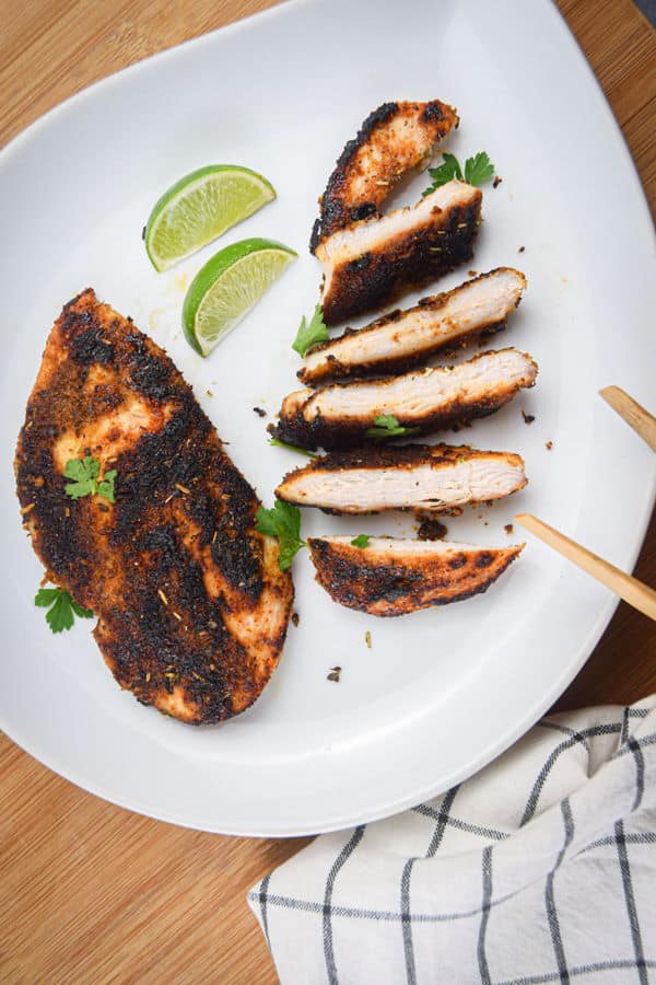 Sliced blackened chicken on a plate with lime wedges.