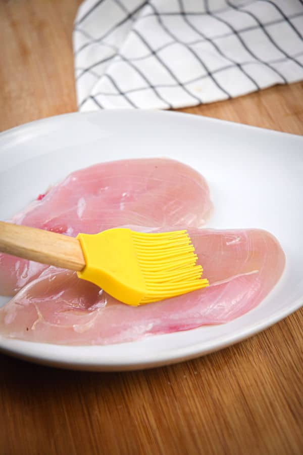 Raw chicken breasts and a silicone brush with oil.