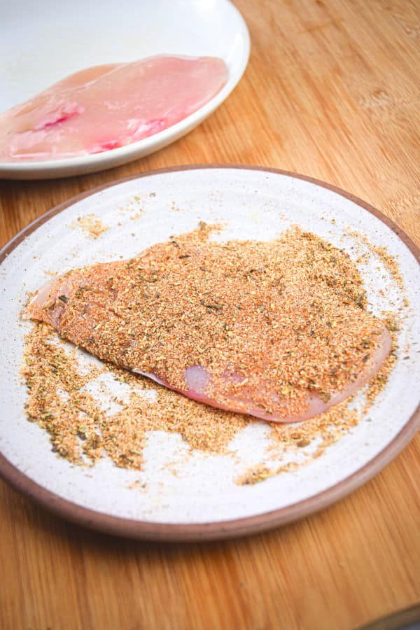 Raw chicken breast on a plate with blackening spices.