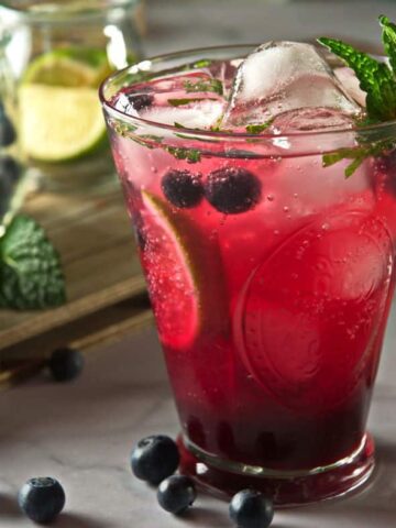 Blueberry mojito mocktail in a glass with fresh blueberries scattered around the glass.