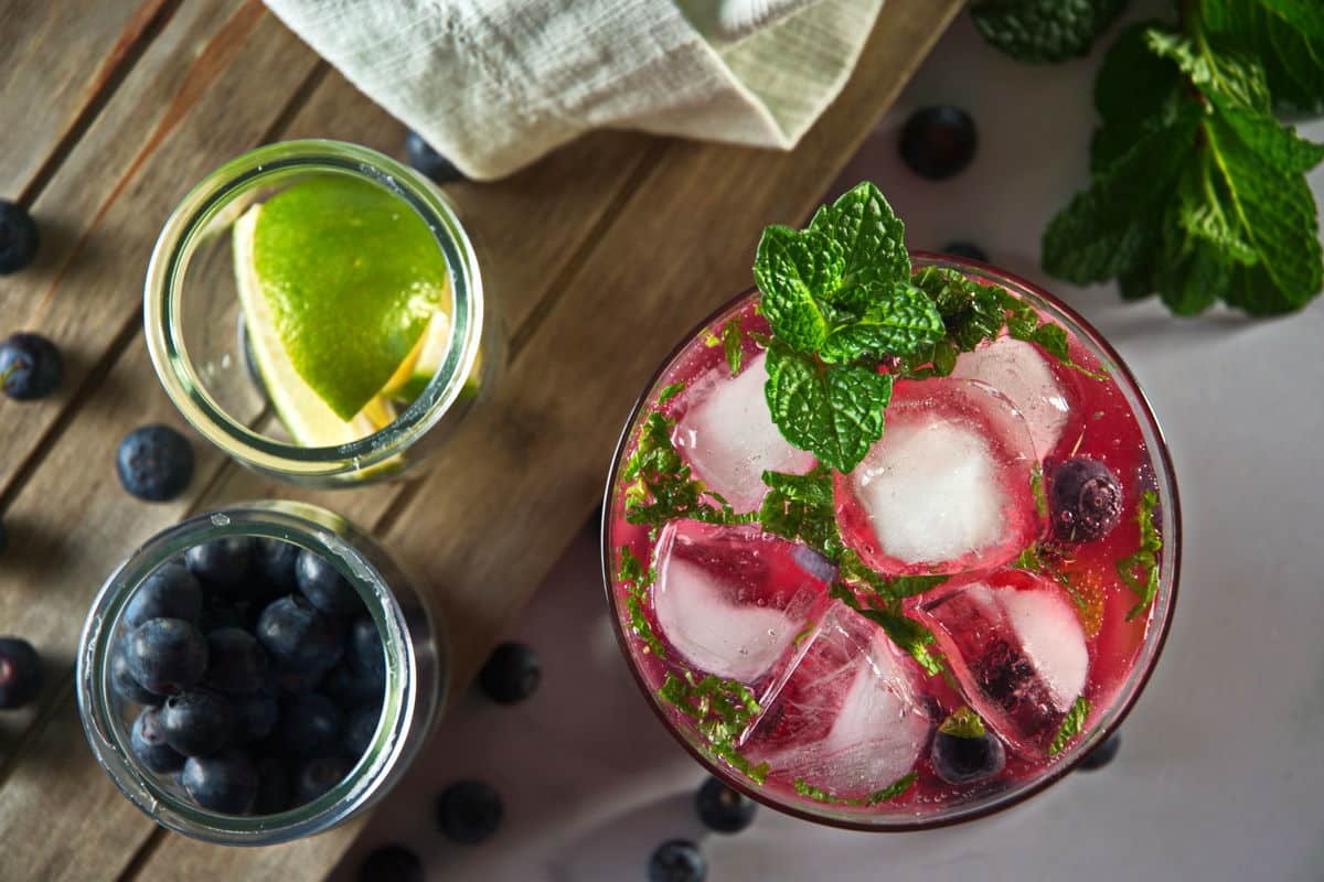 Top view of blueberry mojito mocktail in a glass with limes, blueberries and fresh mint leaves on the side.