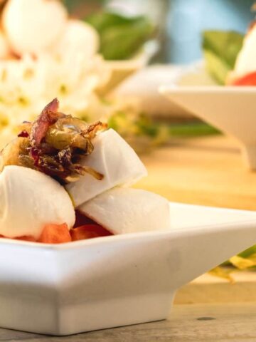 Bocconcini Caprese salad with caramelized onions on white serving dish.