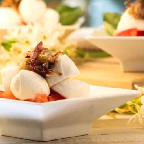 Bocconcini Caprese salad with caramelized onions on white serving dish.