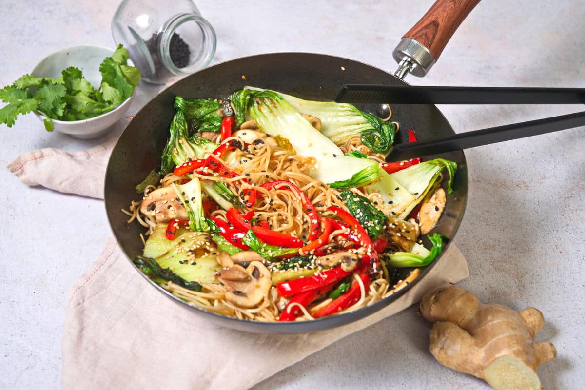 Bok choy stir fry with noodles in frying pan. Chopsticks, ginger root and cilantro on the side.