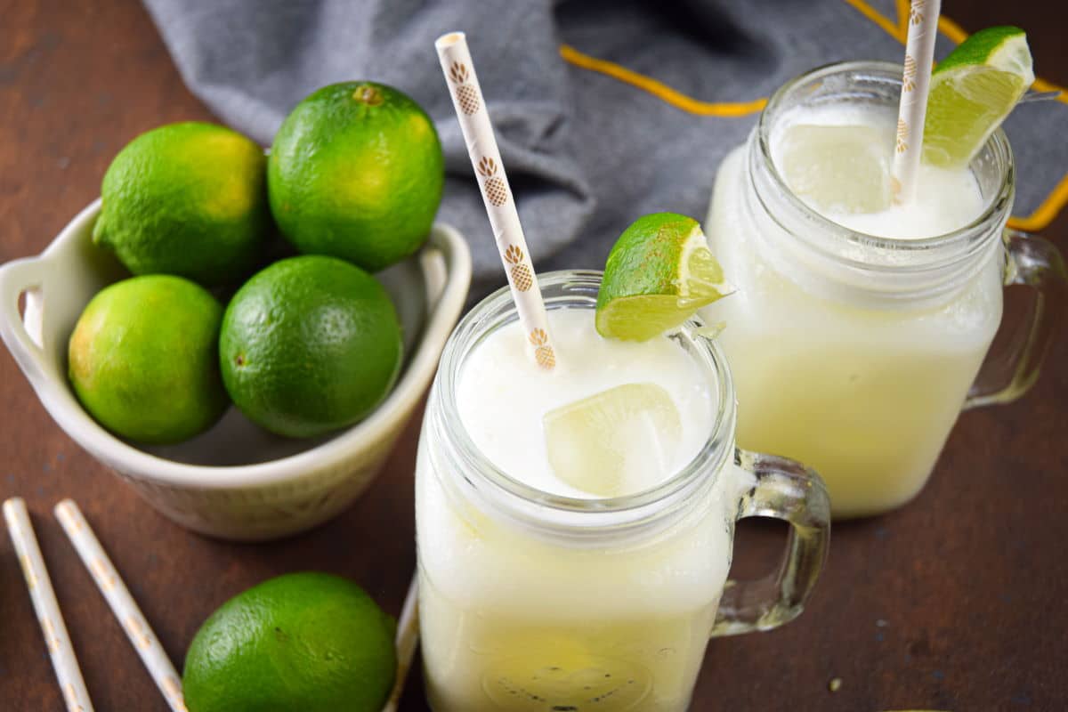 Brazilian lemonade in glass jars with lime wedges and paper straws, limes in a bowl on the side.