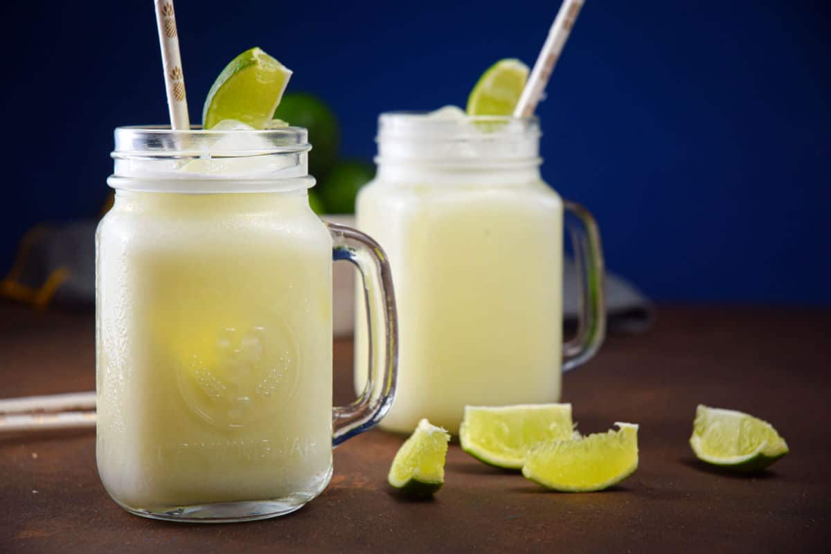Brazilian lemonade in glass jars with lime wedges and paper straws.