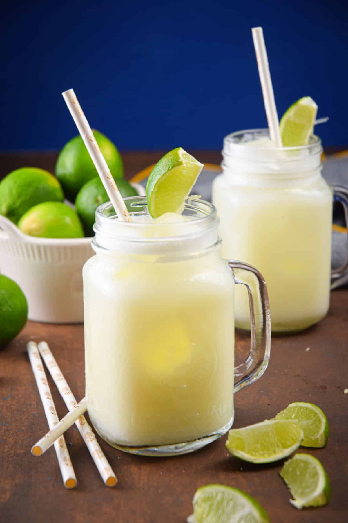 Brazilian lemonade in glass jars with lime wedges and paper straws, limes in a bowl on the side.