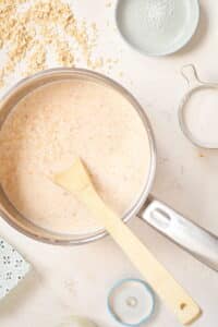 Oats in a pot with water and milk, white background.