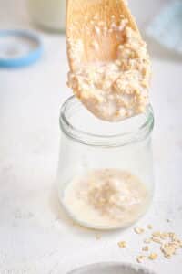 A wooden spoon dipped into a glass jar of oatmeal.
