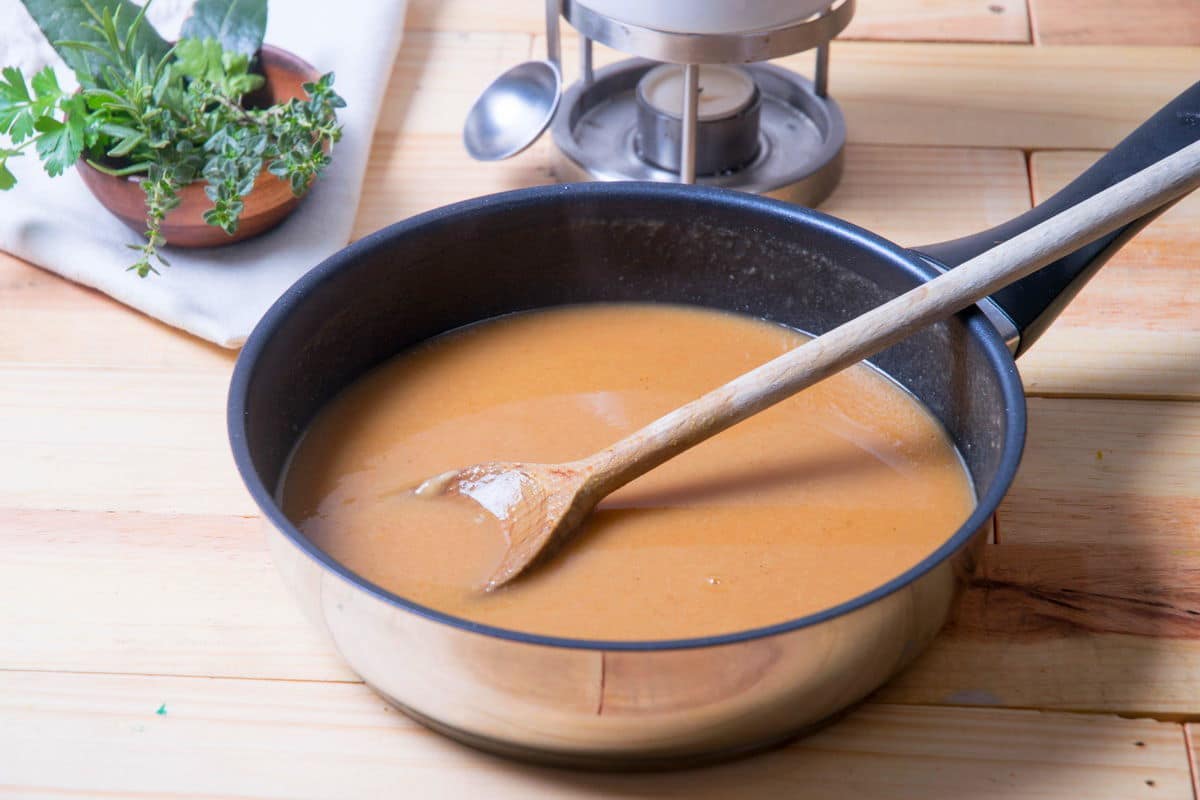 Brown gravy in frying pan on wooden background, gravy warmer in the background.