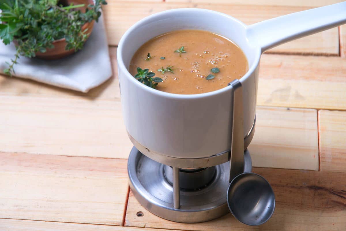 Brown gravy in a gravy warmer on wooden background.