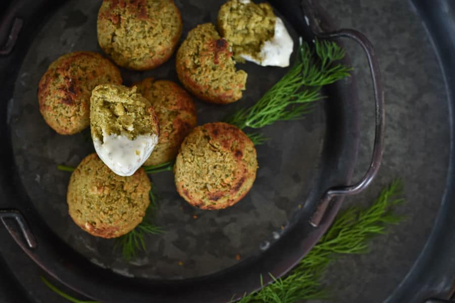 Falafels on a plate with yogurt sauce and fresh dill sprigs.