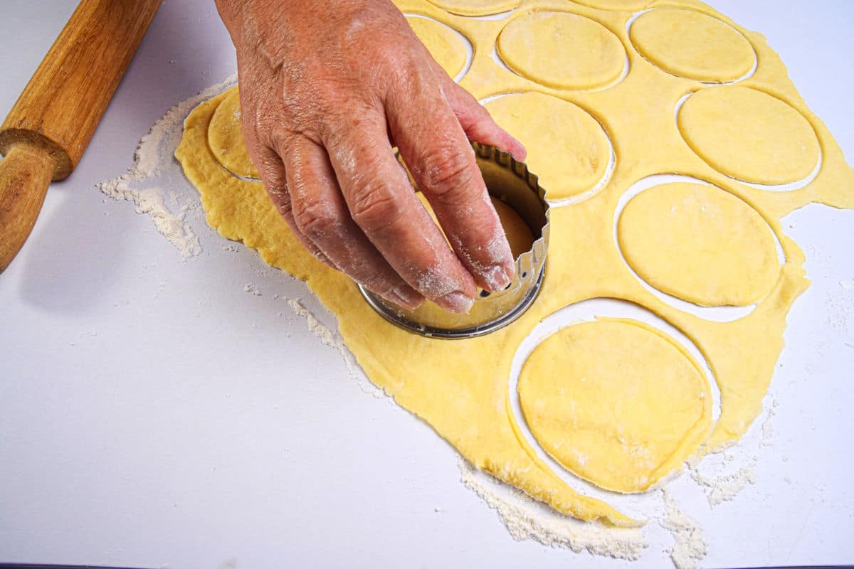 Butter tart pastry cut out into circles on white surface.
