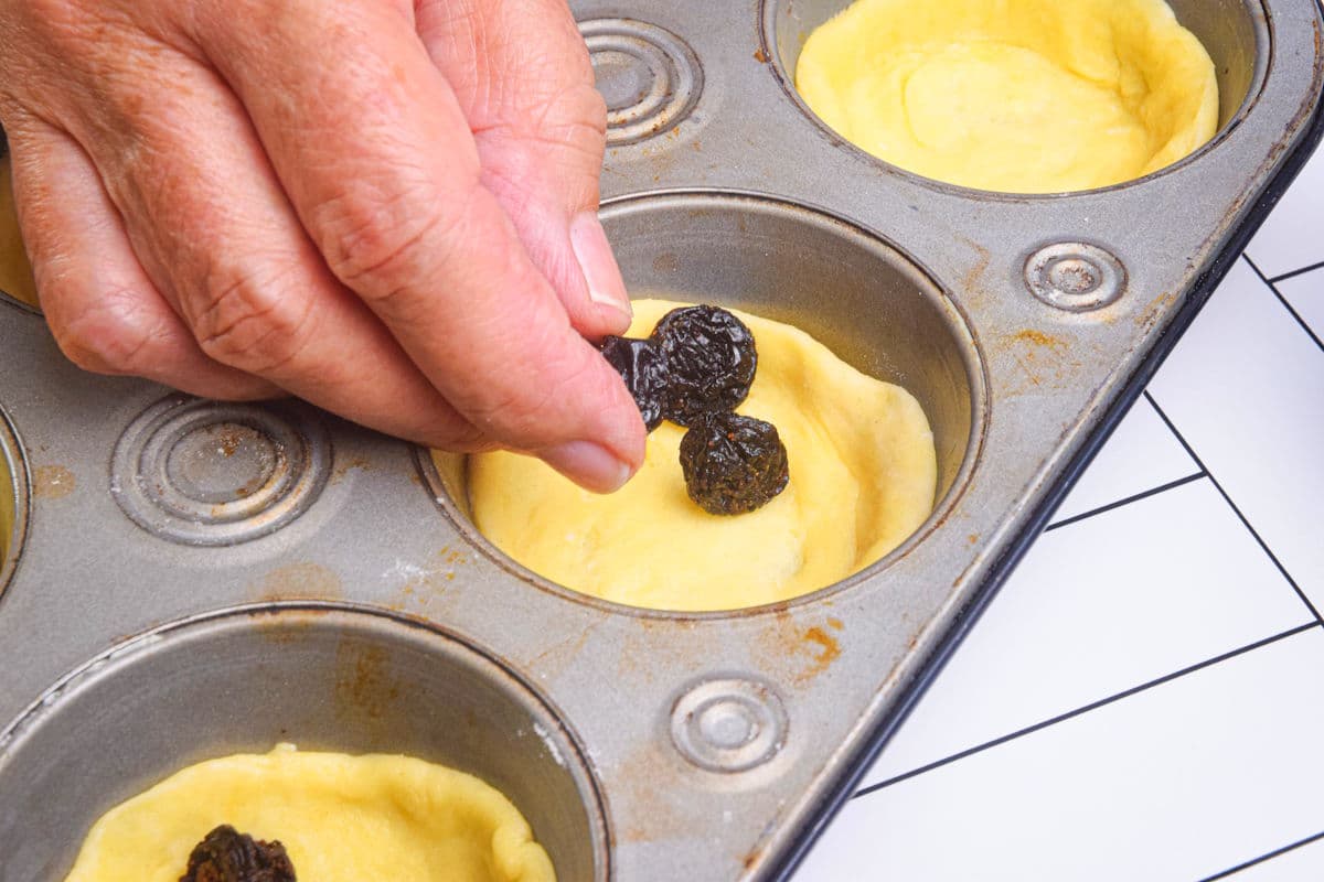 Butter tart pastry and raisins in muffin tin.