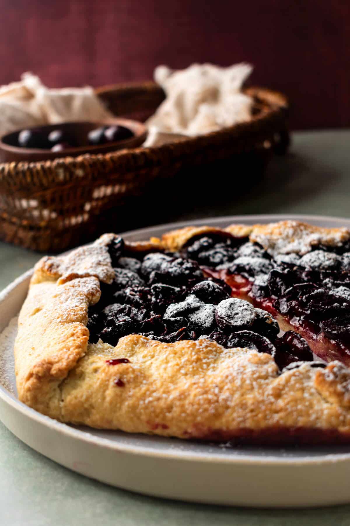 Cherry galette with icing sugar on white plate.