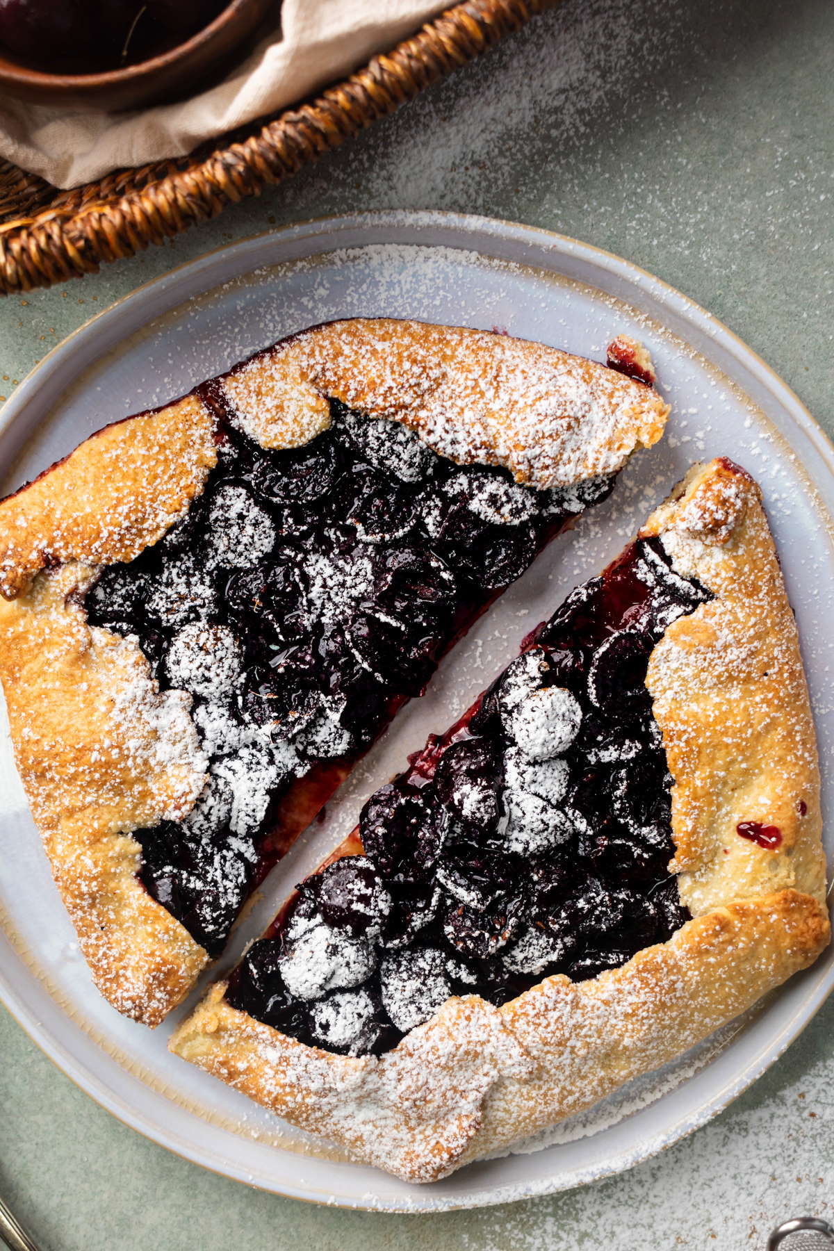 Cherry galette with icing sugar on white plate.