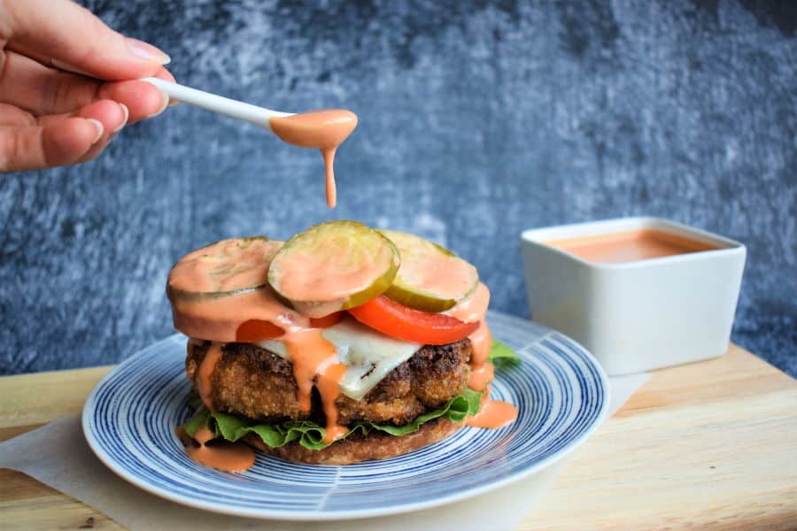 Chicken Fried Beef Burger with side sauce, blue background.