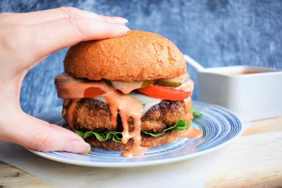 Chicken Fried Beef Burger with side sauce, blue background.