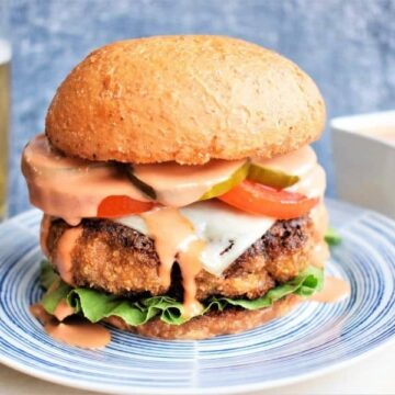 Chicken Fried Beef Burger with side sauce, blue background and glass of beer on the side.