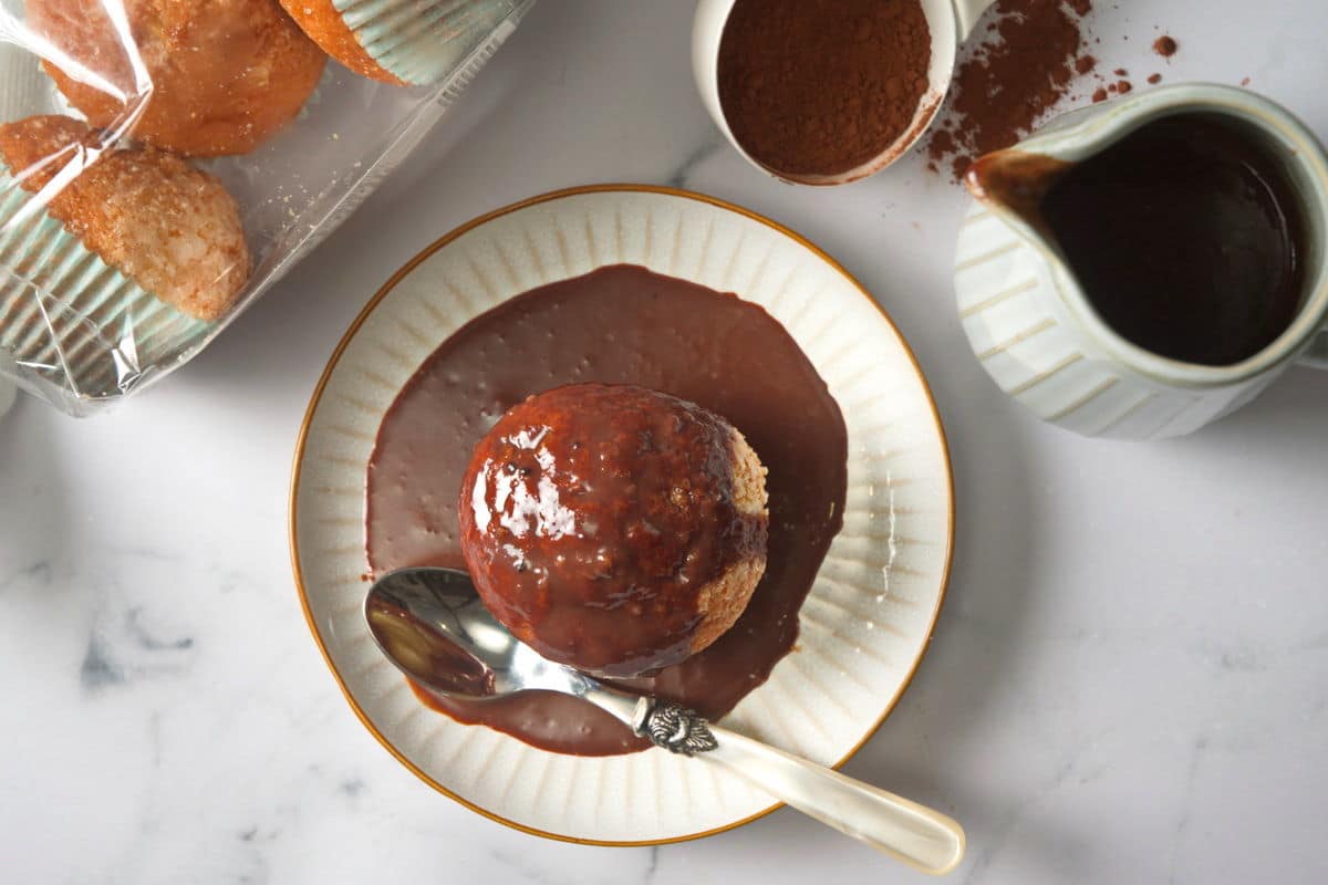 Muffin covered in chocolate gravy on small white plate.