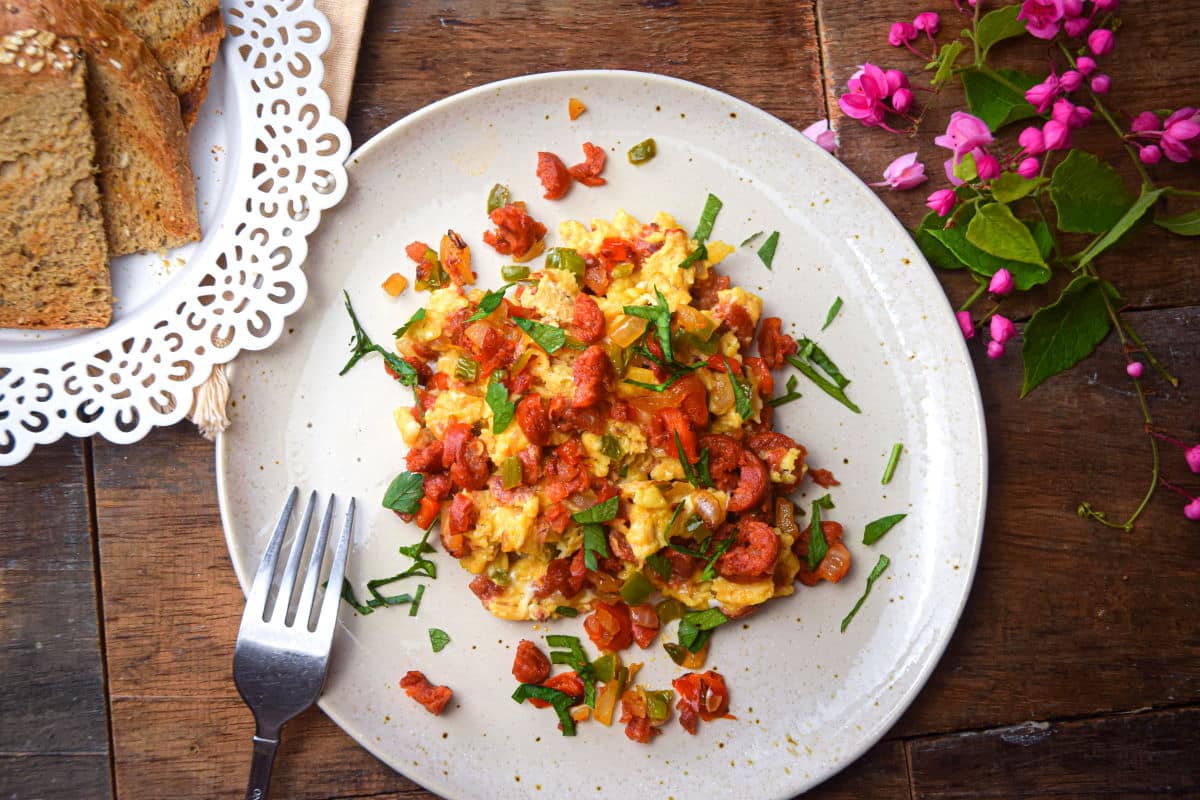 Chorizo and egg scramble on a white plate with toast, small pink flowers scattered on the side.