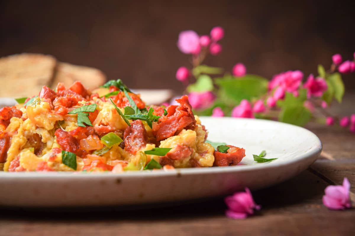 Chorizo and egg scramble on a white plate, small pink flowers scattered on the side.