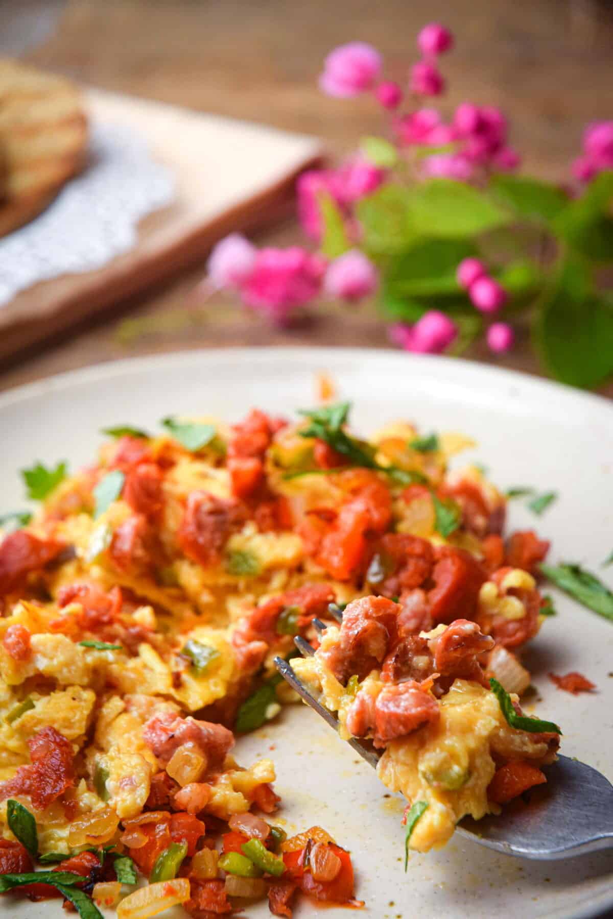 Chorizo and egg scramble on a white plate with a fork, small pink flowers on the side.