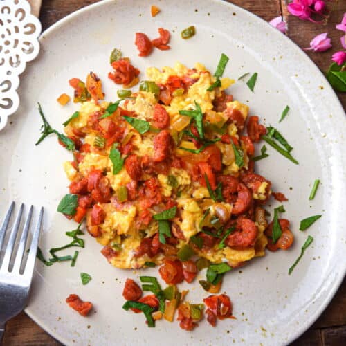 Chorizo and egg scramble on a white plate with toast, small pink flowers scattered on the side.