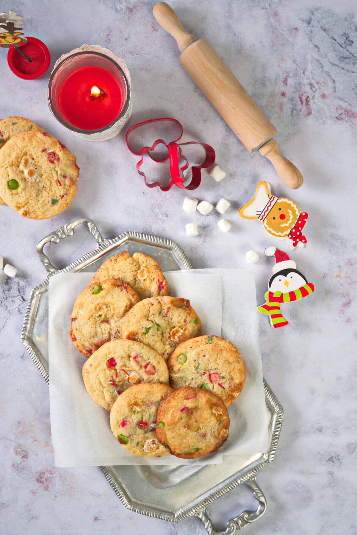 Christmas cookies on a serving tray with a candle, rolling pin and cookie cutters in the background.