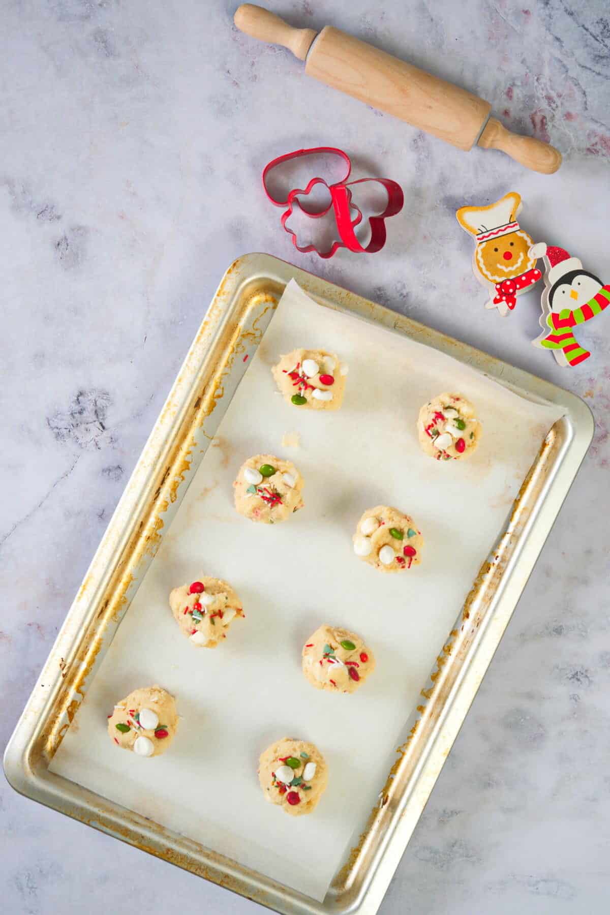 Christmas cookie dough balls on a parchment lined baking sheet, Christmas cookie cutters and rolling pin on the side.