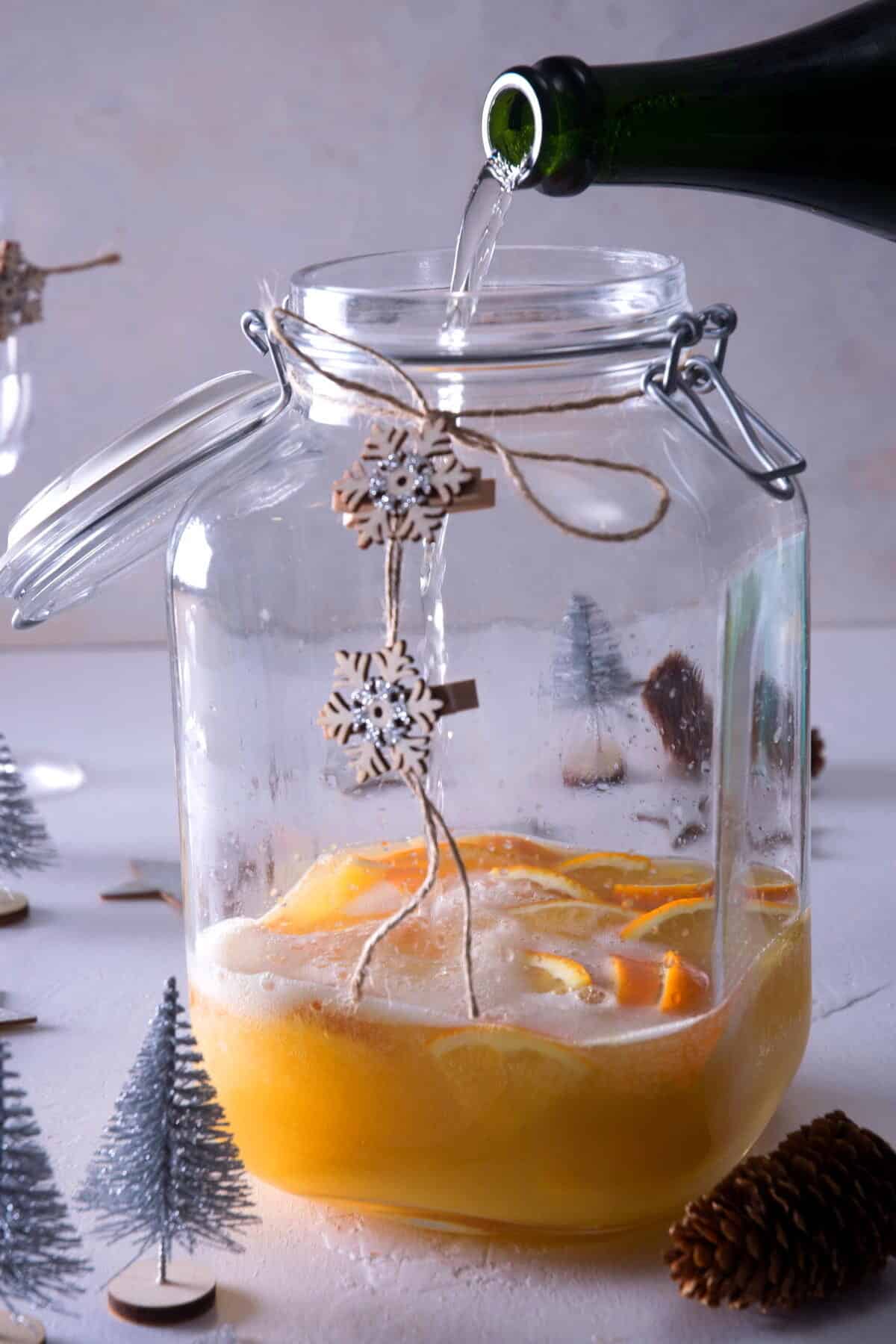 Champagne pouring into a large glass pitcher with orange juice.