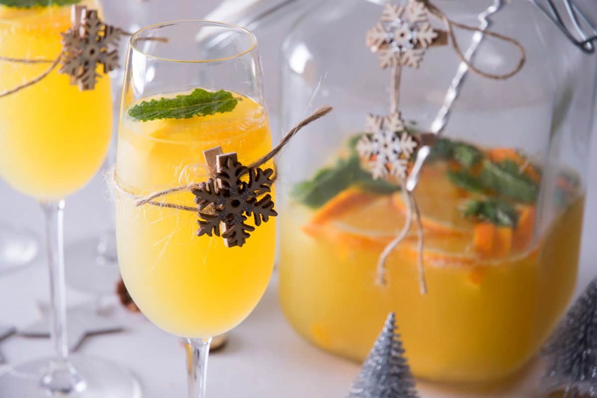Christmas punch in 2 champagne glasses, with a wooden snowflake on each glass, a pitcher in the background.