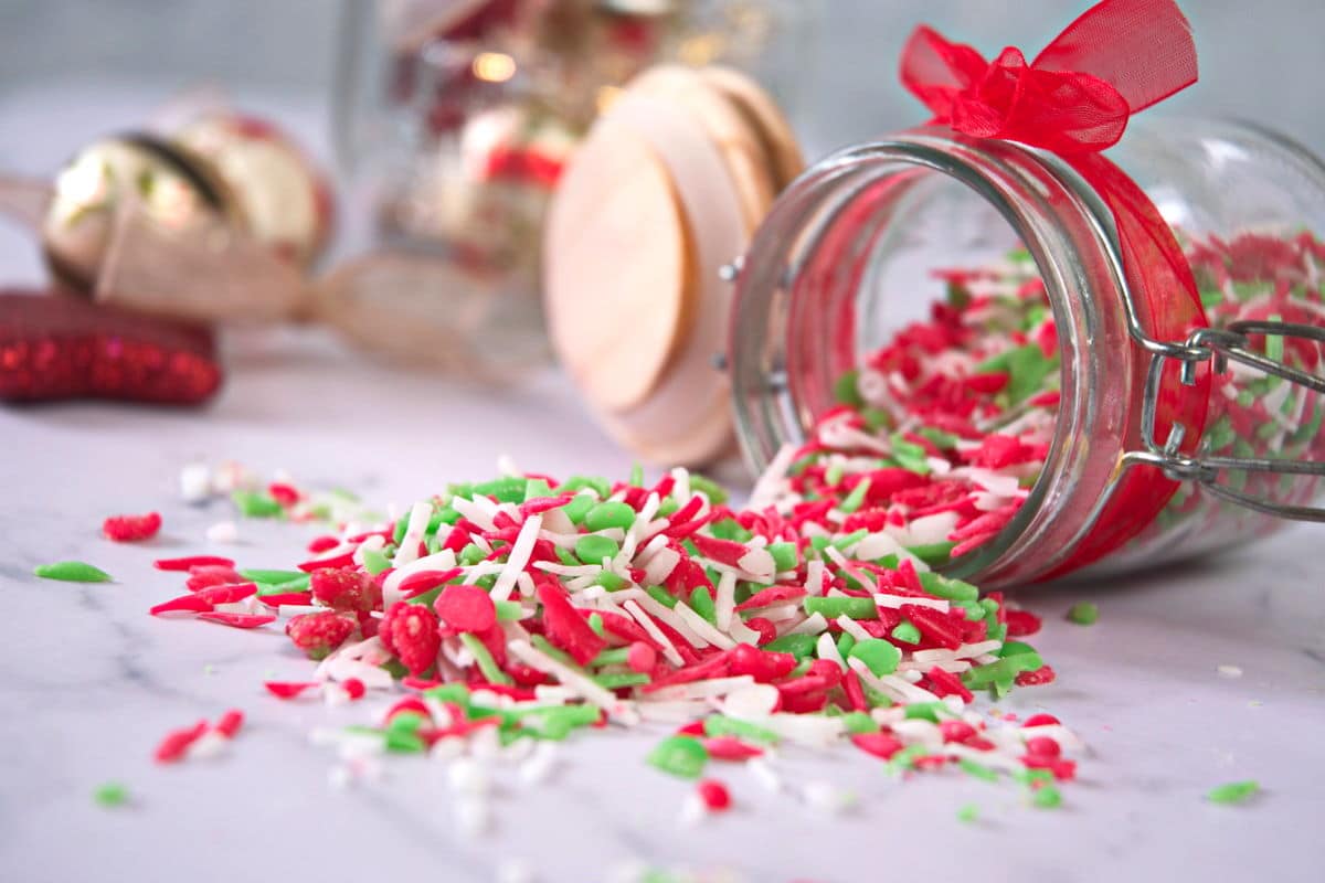 Red, green and white candy sprinkles pouring out of a small glass jar on its side.