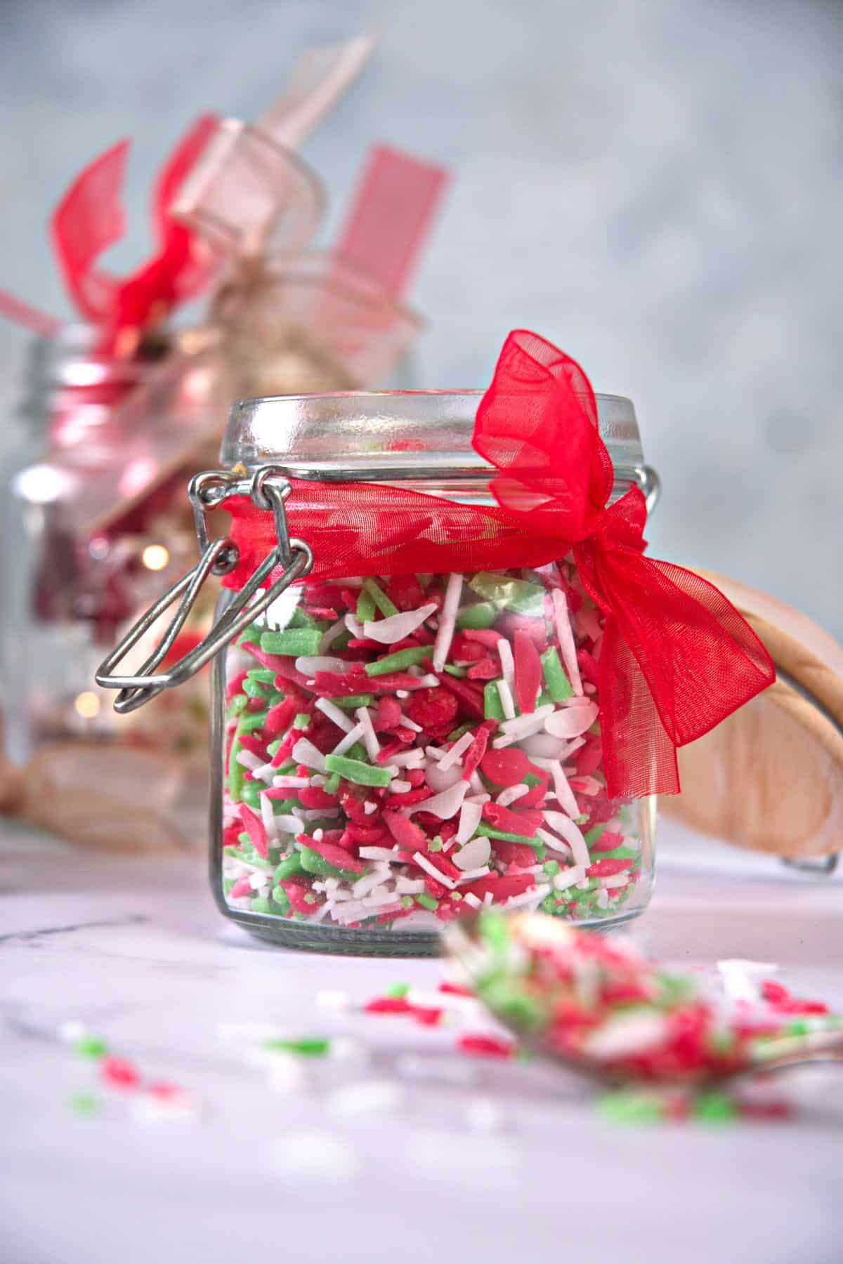 Red, green and white sprinkles in a small jar with a red ribbon.