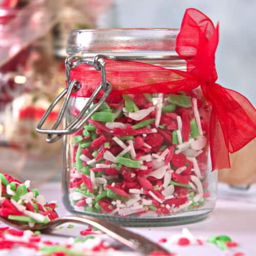 Red, green and white sprinkles in a small jar with a red ribbon.