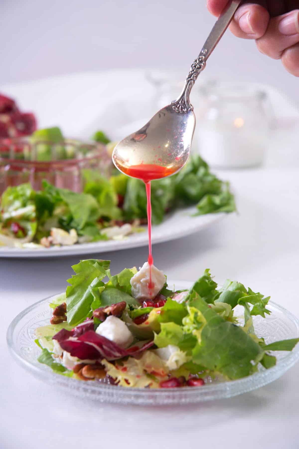 Christmas salad on a small glass plate with pomegranate dressing drizzling over.