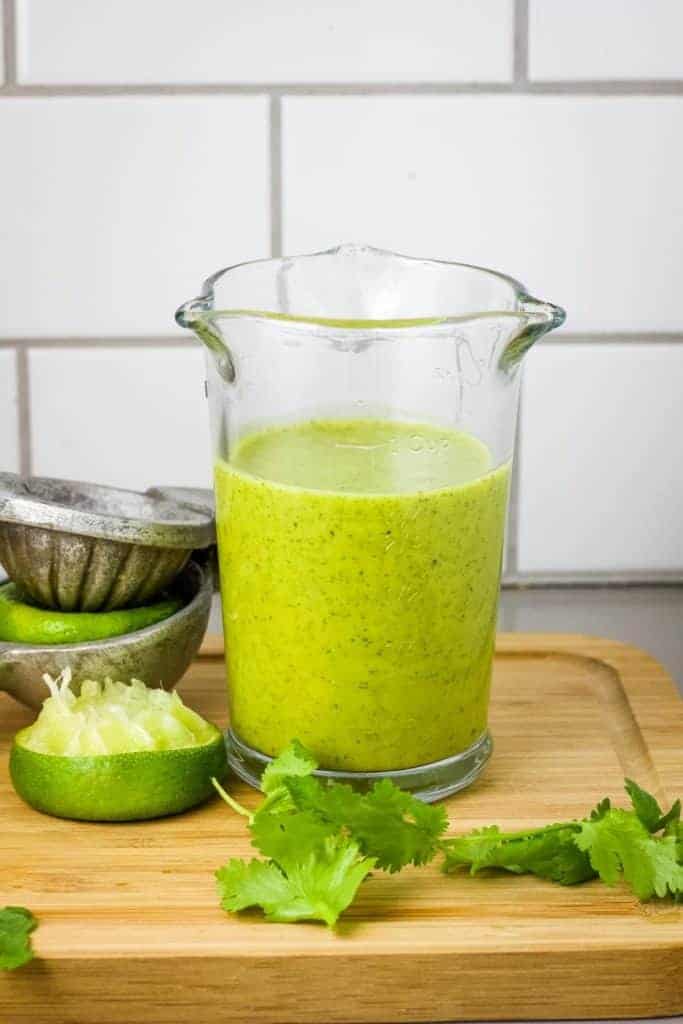 Cilantro lime dressing in glass pitcher on cutting board.