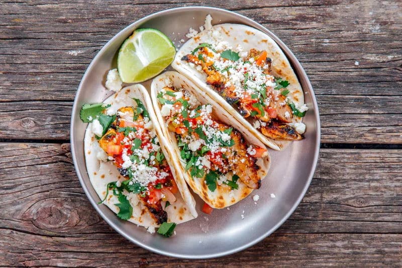 Cilantro chicken tacos on a metal plate on wooden board.