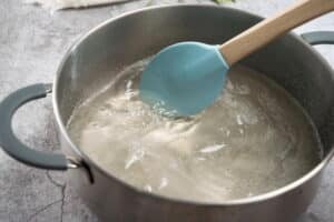 Gelatin water mixture in a large saucepan with a blue spatula.