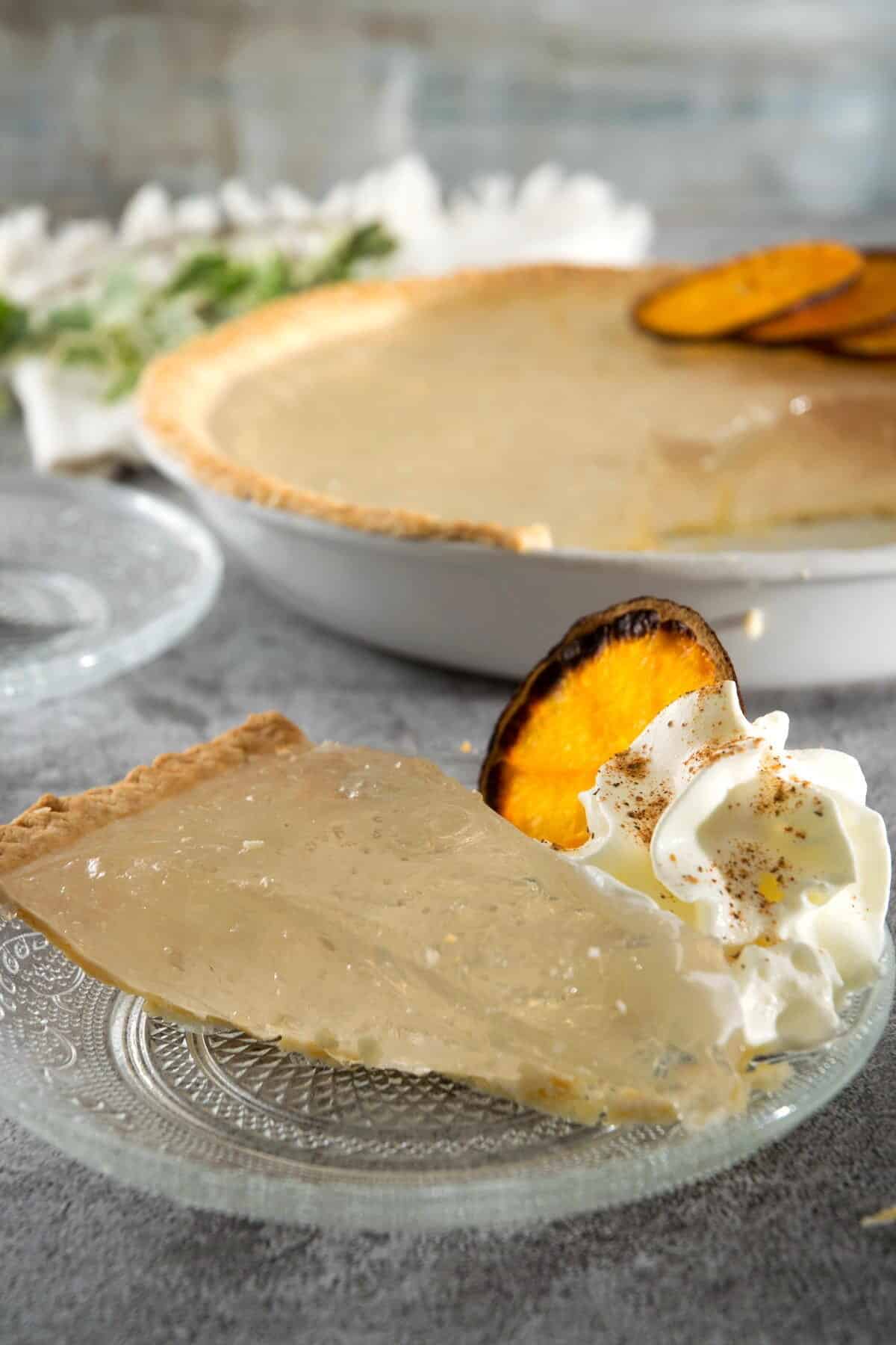 A slice of clear pumpkin pie on a clear glass plate with dehydrated orange slices and whipped cream.