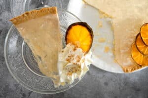 Clear pumpkin pie on a clear glass plate with dehydrated orange slices and whipped cream.