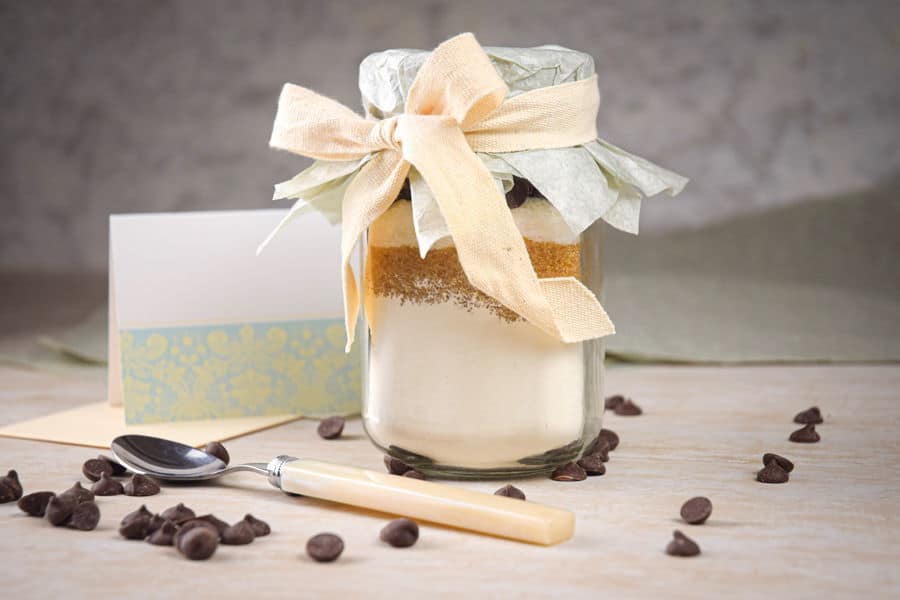 Chocolate chip cookie mix in a jar with chocolate chips, spoon and label on the side.