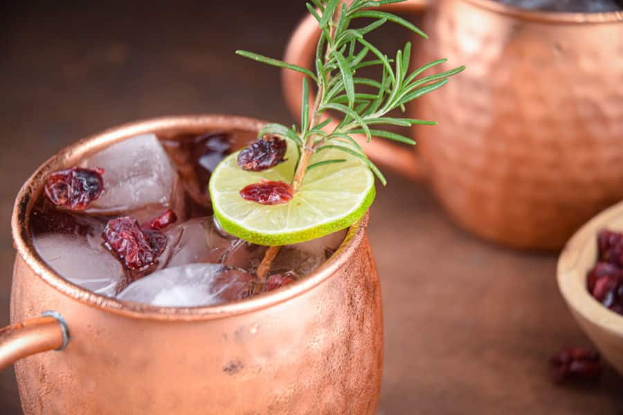 Cranberry Moscow Mule in copper mugs, garnished with cranberries, rosemary and lime slices.