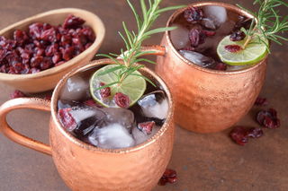 Cranberry Moscow Mule in copper mugs, garnished with cranberries, rosemary and lime slices.